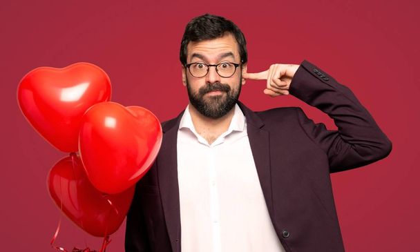 Man in valentine day covering both ears with hands over red background - Photo, Image