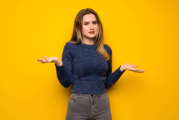 Teenager girl over yellow wall unhappy because not understand something - Foto, Bild
