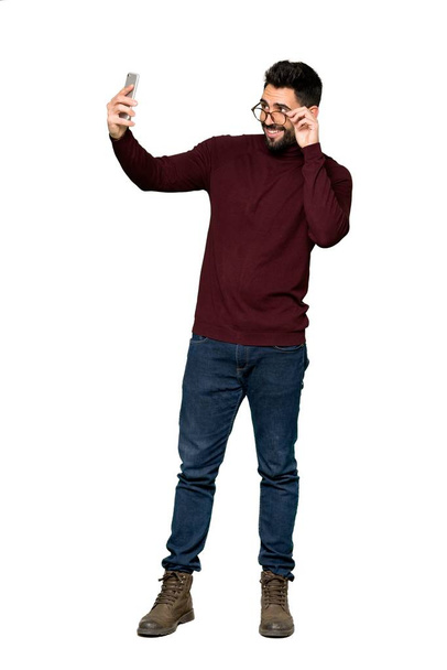 Tiro completo de homem bonito com óculos fazendo uma selfie em fundo branco isolado
 - Foto, Imagem