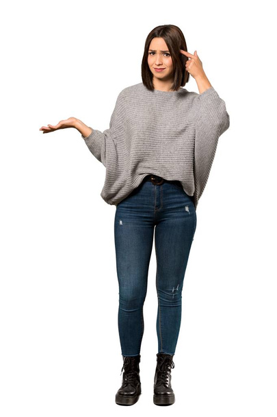 A full-length shot of a Young woman making the gesture of madness putting finger on the head over isolated white background - Photo, Image