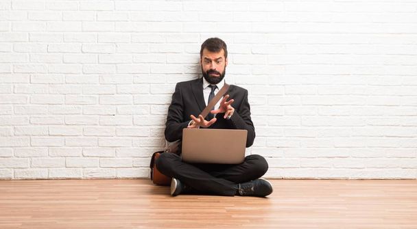 Бізнесмен з ноутбуком, що сидить на підлозі, трохи нервує і боїться розтягувати руки на передній план
 - Фото, зображення