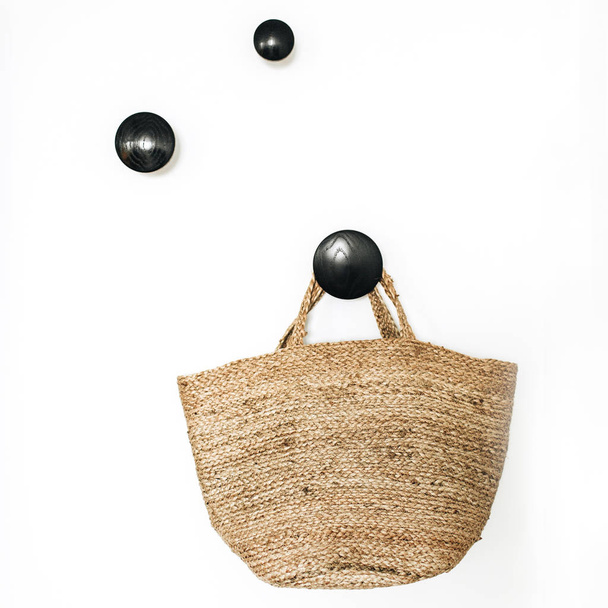 Καλάθι ψάθινο τσάντα σε μαύρο κρεμάστρα σε λευκό φόντο. Έννοια του σύγχρονου Σκαδιναβικού design. - Φωτογραφία, εικόνα