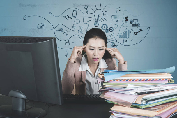 Bild einer gestressten Geschäftsfrau, die einen Stapel Dokumente betrachtet, während sie im Atelier überarbeitet  - Foto, Bild