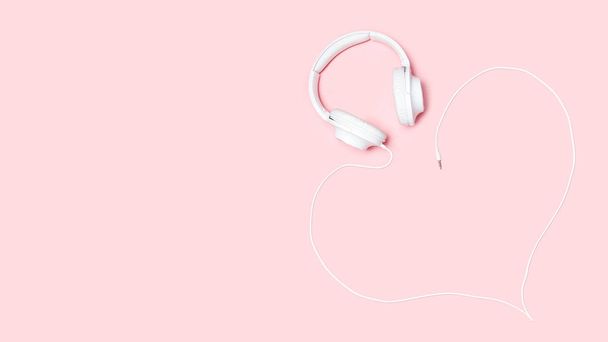 Hoofdtelefoon met een koord in de vorm van een hart op roze achtergrond. Minimalistische plat leggen samenstelling met kopie ruimte voor bloggers, ontwerpers, tijdschriften etc - Foto, afbeelding