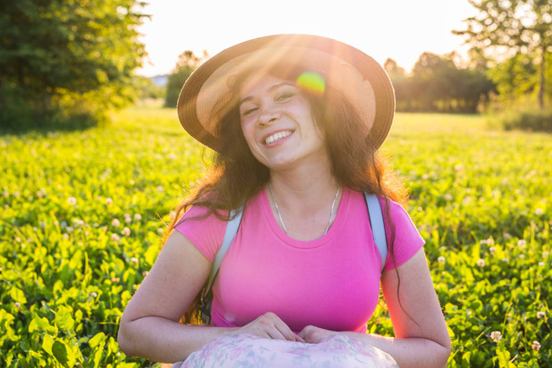 Summer and nature concept - Healthy smiling young woman lying on green grass with wildflowers. She is laughing and happy - Foto, imagen