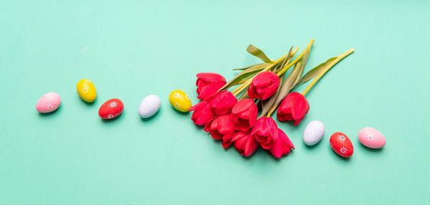 Easter eggs, pastel colors painted and red tulips bouquet, green background, banner, copy space - Foto, imagen