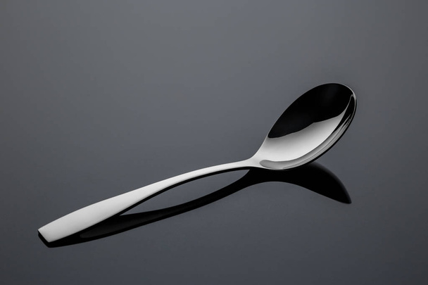Stainless steel metal spoon on a reflective surface - Foto, Imagem