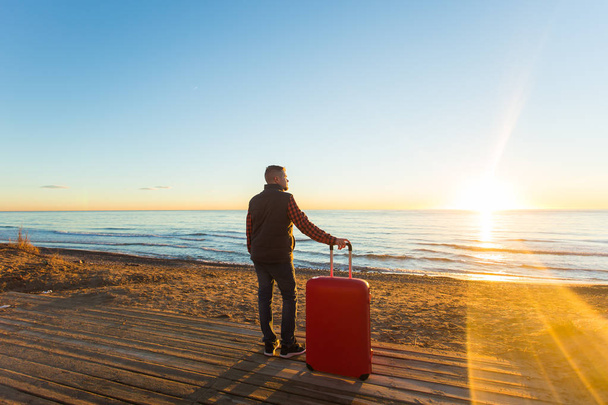Vakantie, reizen en toerisme concept - knappe man met rode koffer over zandstrand achtergrond - Foto, afbeelding