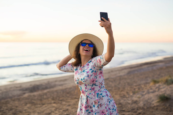 Подорожі, відпустка та концепція людей - молода жінка в капелюсі та окулярах, що приймає селфі на пляжі
 - Фото, зображення