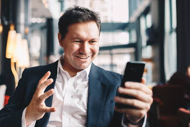 Attractive young man in a bar getting good results over an email on his mobile phone. He is celebrating by raising his hand in the air. - Zdjęcie, obraz