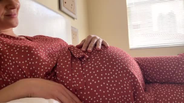 Mladá těhotná žena hladí břicho s láskou přičemž odpočinek ve špatné. Detail z velkých těhotné bříško. - Záběry, video
