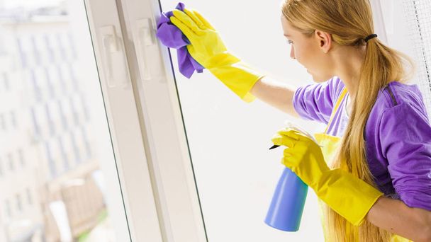 Young housewife cleaner woman washing window at home using cloth and spray detergent. Cleaning concept - Foto, Bild