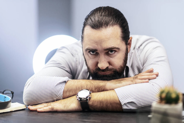 Dark-haired bearded man in a striped shirt feeling tired - Fotoğraf, Görsel