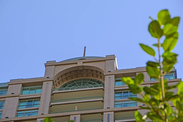 Low angle view of beautiful building against blue sky with green tree branch on blurred foreground - Photo, Image