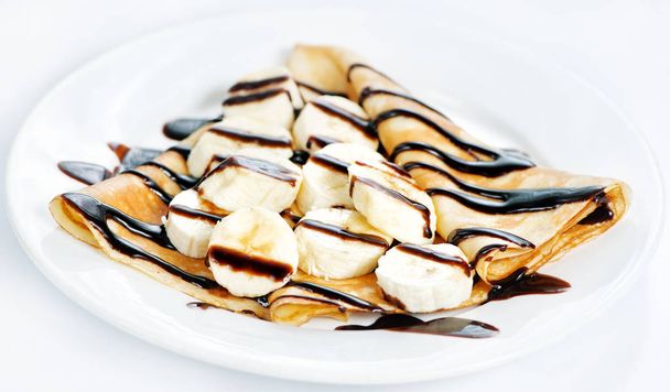バナナとチョコレートの白い背景がある薄いおいしいパンケーキ - 写真・画像