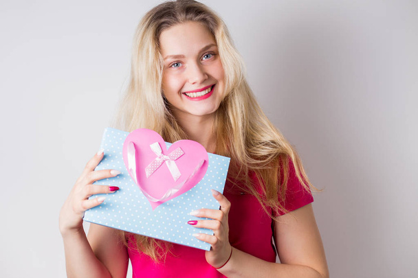 Portrait of beautiful smiling blonde woman with gift bag, package on hands on white background. Positive emotions, joy, happiness, birthday, Valentine's day, holiday concept - Zdjęcie, obraz