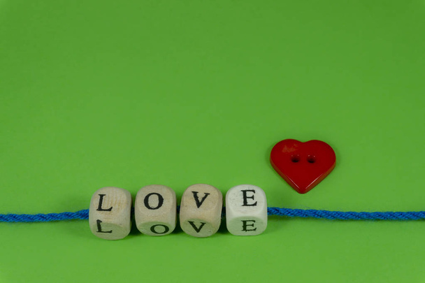 Rode hartvormige knop en het woord Love on blokken schroefdraad op snaren over een kleurrijke groene achtergrond voor romantisch of Valentines concepten met presentexemplaar ruimte voor tekst - Foto, afbeelding