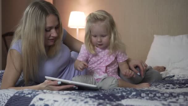 Μια γυναίκα και ένα παιδί με έναν υπολογιστή tablet στο κρεβάτι. - Πλάνα, βίντεο