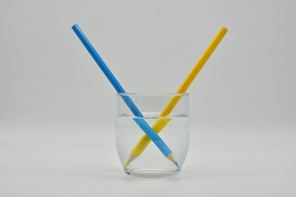 Refraccion de la luz, demostrada en una vaso de agua con lapices de colores. - Foto, Imagen