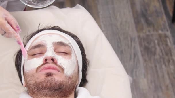 Concetto di spa per uomini. Un giovane uomo viene applicata una maschera cosmetica sul viso in un salone di bellezza
 - Filmati, video