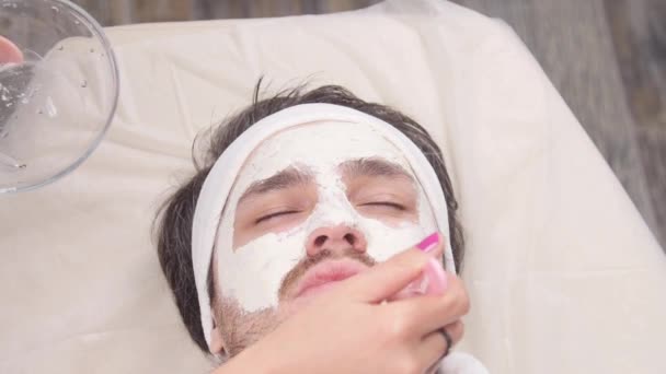 Koncepcja spa dla mężczyzn. Młody człowiek jest stosowana kosmetycznych maski na twarzy w gabinecie kosmetycznym - Materiał filmowy, wideo