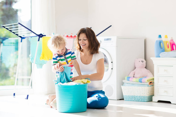 Mutter und Kinder in Waschküche mit Waschmaschine oder Wäschetrockner. Hausarbeit. moderne Haushaltsgeräte und Waschmittel in weißen, sonnigen Wohnungen. sauber gewaschene Kleidung auf dem Wäscheständer.  - Foto, Bild
