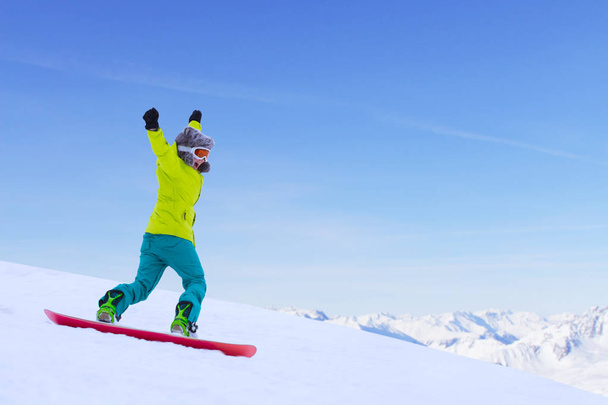 Girl snowboarder running down the slope in Alpine mountains. Winter sport and recreation, leisure outdoor activities. Image of excited screaming young woman enjoyment concept - Photo, Image