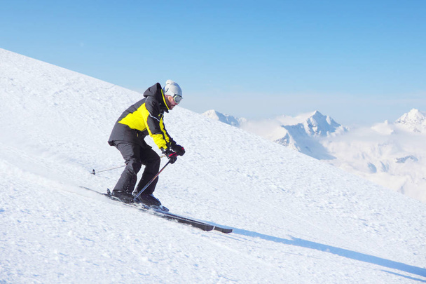 Alpine skier on piste running downhill in beautiful Alpine landscape. Blue sky on background. Free copy space for text - Zdjęcie, obraz