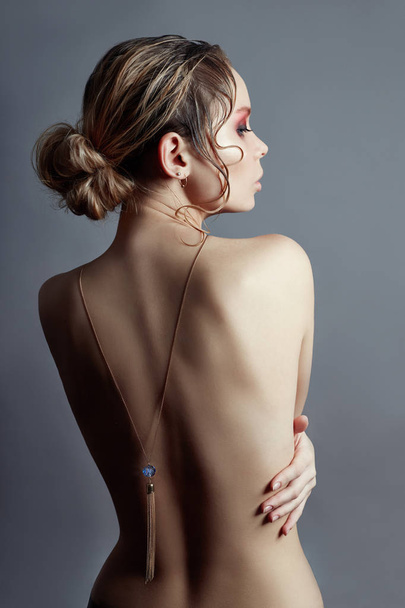 Art of Nude fashion Nude back blonde on grey background, pendant necklace on chain on back. The girl hugs her hands. Beauty and skin care perfect body - Fotografie, Obrázek