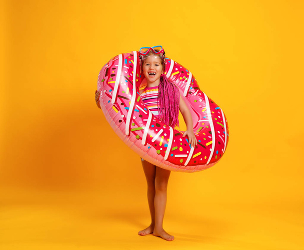 gelukkig kind meisje in zwembroek met ring donut zwemmen over een gekleurde gele pagina - Foto, afbeelding