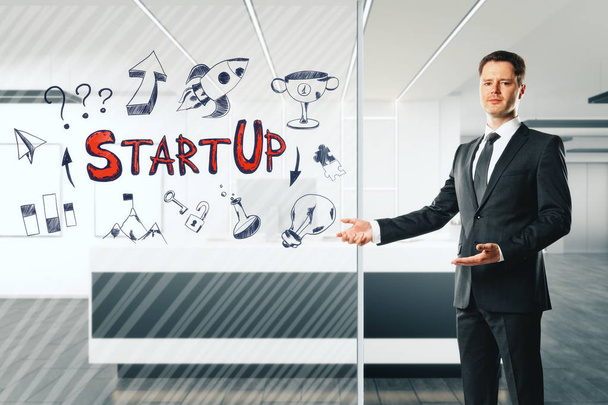 Houkutteleva nuori liikemies seisoo toimistossa vastaanotto sisustus startup luonnos lasia. Käynnistys- ja menestyssuunnitelma
. - Valokuva, kuva
