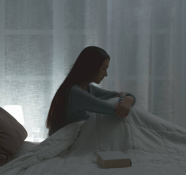 Sad depressed woman lying in bed late at night, she is suffering from insomnia and feels exhausted - 写真・画像