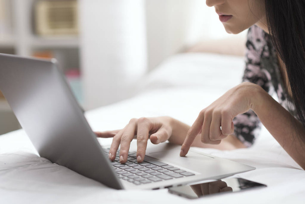 Young woman lying on the bed at home and working with her laptop, lifestyle and technology concept - Foto, imagen