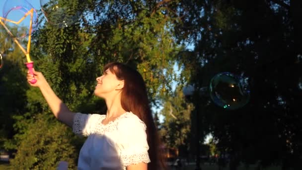 Girl blows big soap bubbles and laughs while walking in park. Slow motion. Summer walks and games in nature. - Footage, Video