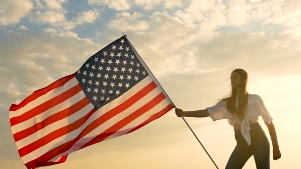Chica de pelo largo adolescente de pie con bandera americana contra el cielo con nubes. Movimiento lento
 - Metraje, vídeo