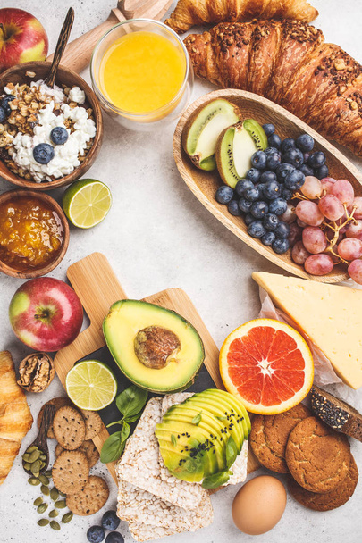 Healthy balanced breakfast on a white background. Muesli, juice, croissants, cheese, biscuits and fruit, top view. - Foto, Imagem