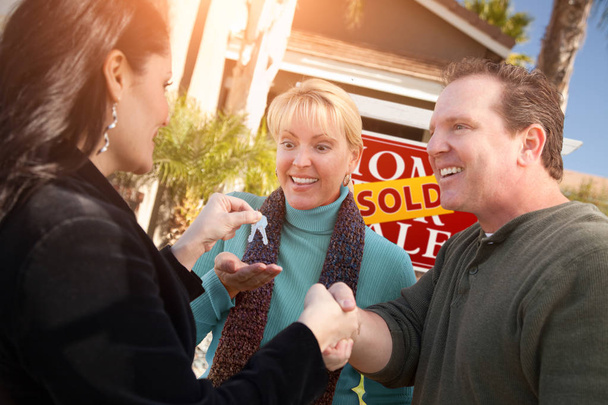 Латиноамериканская женщина-агент по недвижимости передает ключи от нового дома счастливой паре перед продажей знака "Недвижимость"
. - Фото, изображение