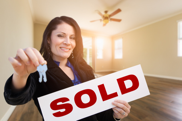 Hiszpanin kobieta z klucze do domu i znak sprzedawanych nieruchomości w pustym pokoju w domu. - Zdjęcie, obraz