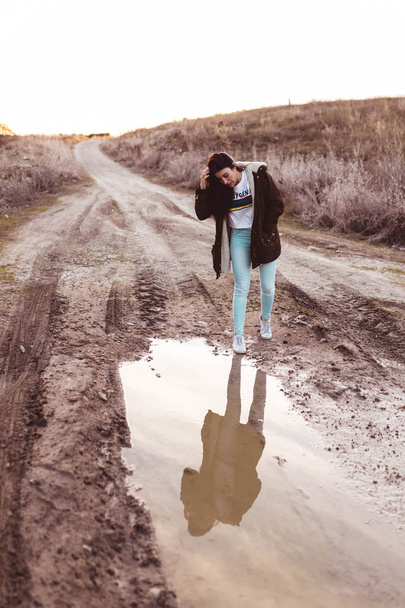 young woman looking in the puddle at sunset in the countryside - Foto, afbeelding