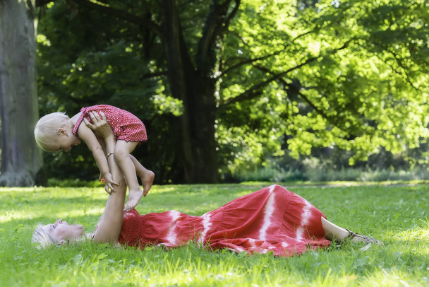 Mère aux cheveux blonds jouant avec un enfant dans un parc d'été
 - Photo, image