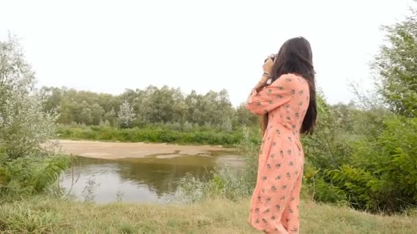 Ein brünettes Mädchen mit langen Haaren fotografiert den Fluss. Zeitlupe. schöne Landschaft - Filmmaterial, Video
