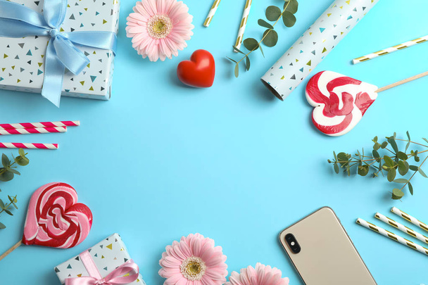Composición plana con flores de gerberas, caja de regalo y caramelos sobre fondo azul. Espacio para texto
 - Foto, Imagen