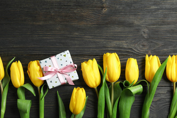 Beautiful yellow tulips and gift on wooden background, space for text. Top view - 写真・画像