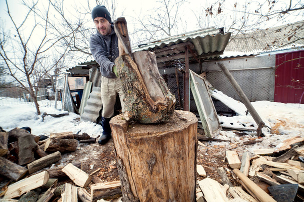 A lumberjack chops wood for a stove in a house for the cold season - Photo, Image