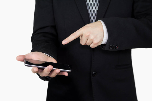 Businessman in Black Suit and Tie Holding Smartphone in Hand And Pointing Finger at Phones Screen Against White Background - Photo, Image