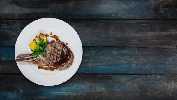Rib-eye steak with corn rotating on a white plate. Top view on a wooden background. Copy space for your text. - Footage, Video