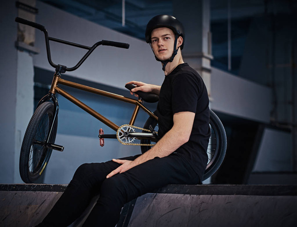 Bmx rider se détendre après avoir pratiqué des tours avec son vélo dans un skatepark à l'intérieur
 - Photo, image