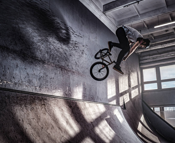 Young BMX making crazy tricks on his bicycle in skatepark indoors. - Photo, Image