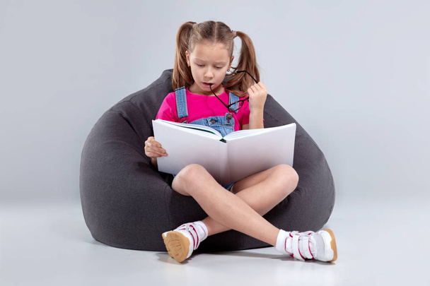 Young girl in glasses reading a book on a gray bean bag - Фото, зображення
