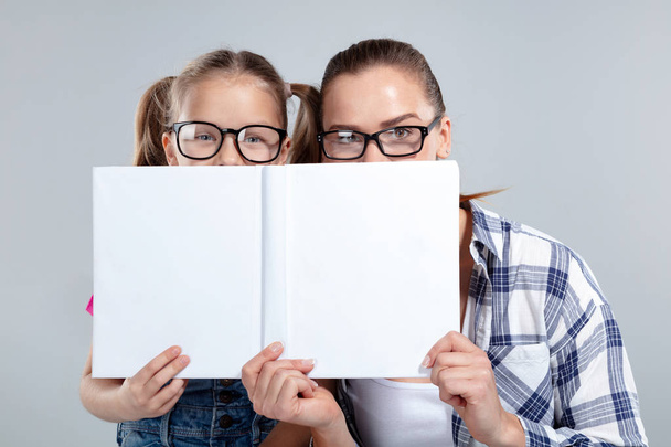 Smiling beautiful woman and her daughter in glasses with book - Foto, imagen